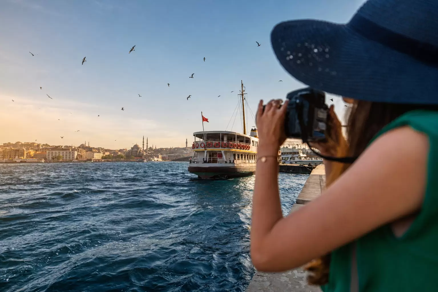 A woman in a sun hat photographing an Istanbul ferry on the Bosphorus.